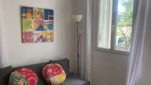 Ein Wohnzimmer mit grauem Sofa, zwei farbenfrohen Kissen, einem weißen Tisch und einer Stehlampe.