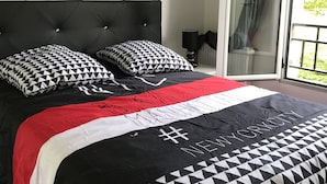 A bedroom with a large bed, a black headboard, and a view of the outdoors through a sliding glass door. - Disneyland paris esprit (Bussy-Saint-Georges)