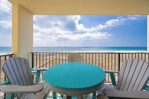 Un balcone con un tavolo color turchese e poltrone Adirondack vista spiaggia.