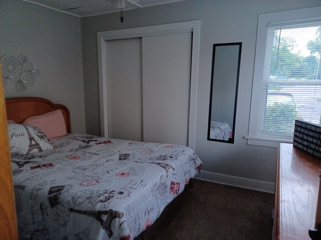 Un dormitorio con una cama, un armario, un espejo y una ventana con persianas.