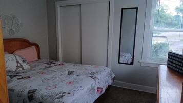 Un dormitorio con una cama, un armario, un espejo y una ventana con persianas.