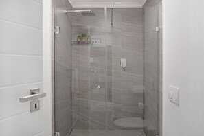 Une douche moderne avec une porte en verre, une petite étagère avec des plantes et des toilettes visibles à travers le verre.