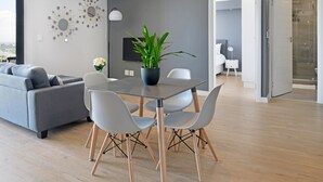 En moderne stue med en grå sofa, et spisebord med fire stole, en potteplante og et fladskærms-TV på væggen.
