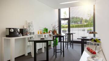 A modern kitchen with white cabinetry, a coffee machine, and a fruit display.