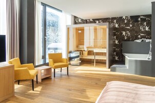Una habitación de hotel moderna con una cama grande, un escritorio, una silla y vistas al exterior a través de amplias ventanas.
