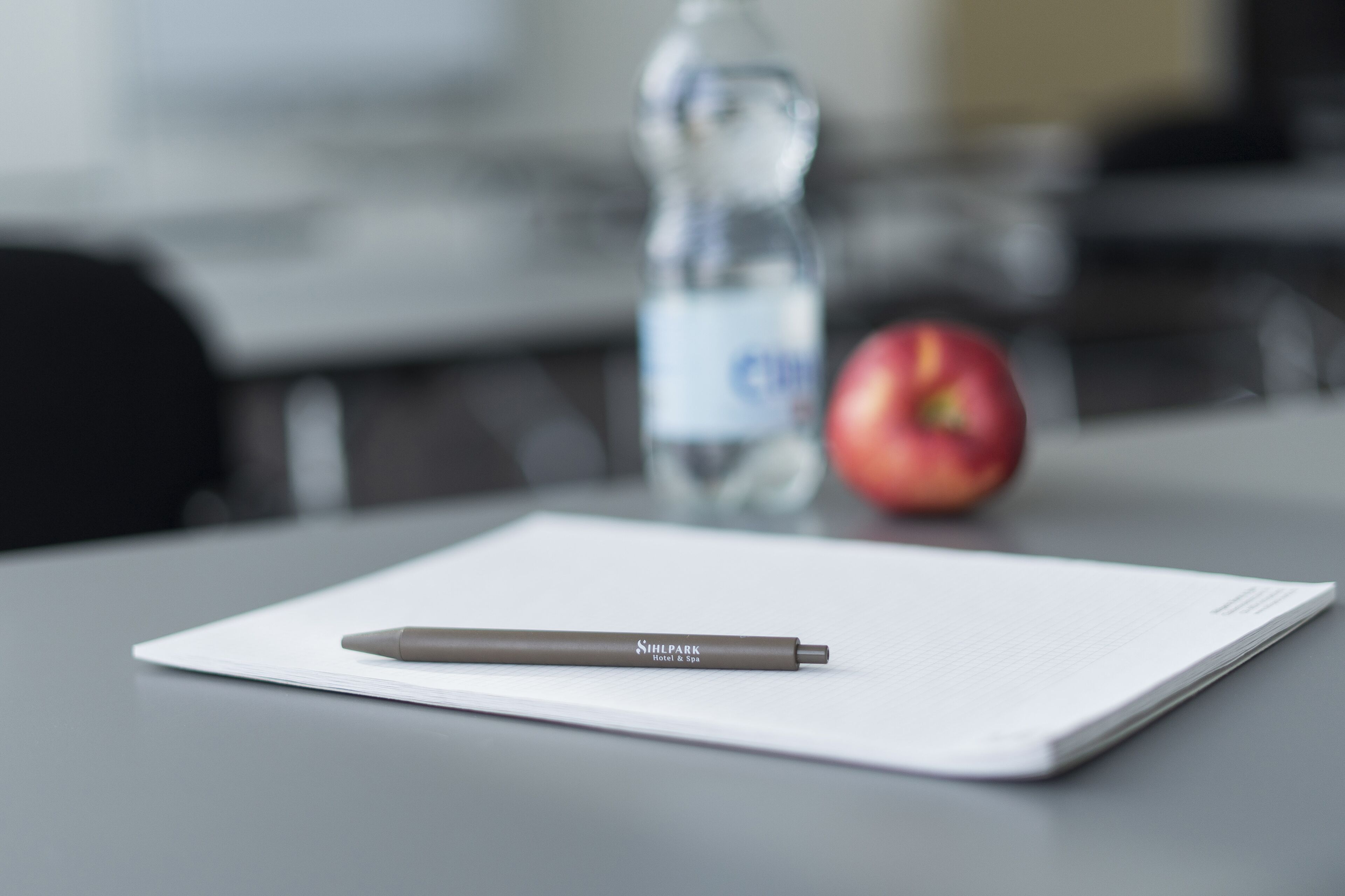 A pen on a white sheet of paper, a bottle of water, and an apple on a table.