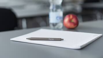 A pen on a white sheet of paper, a bottle of water, and an apple on a table.
