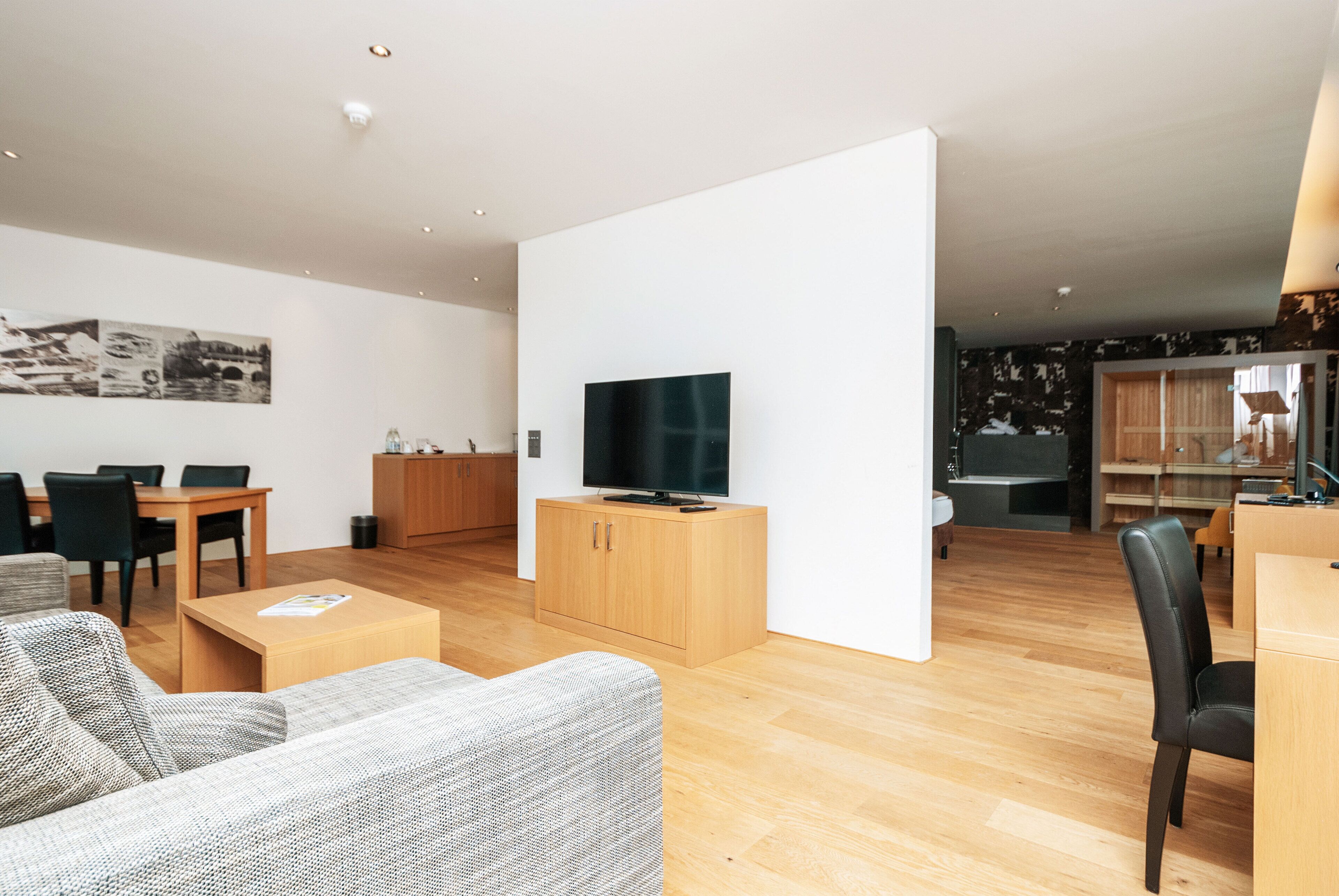 Ein modernes Wohnzimmer mit Flachbildfernseher, Holzkredänzen und einem Essbereich mit Tisch und Stühlen.