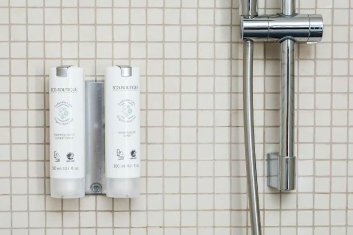 Dos botellas de artículos de aseo con la etiqueta 'Eco-Boutique' sobre una pared de azulejos con una ducha de acero inoxidable.