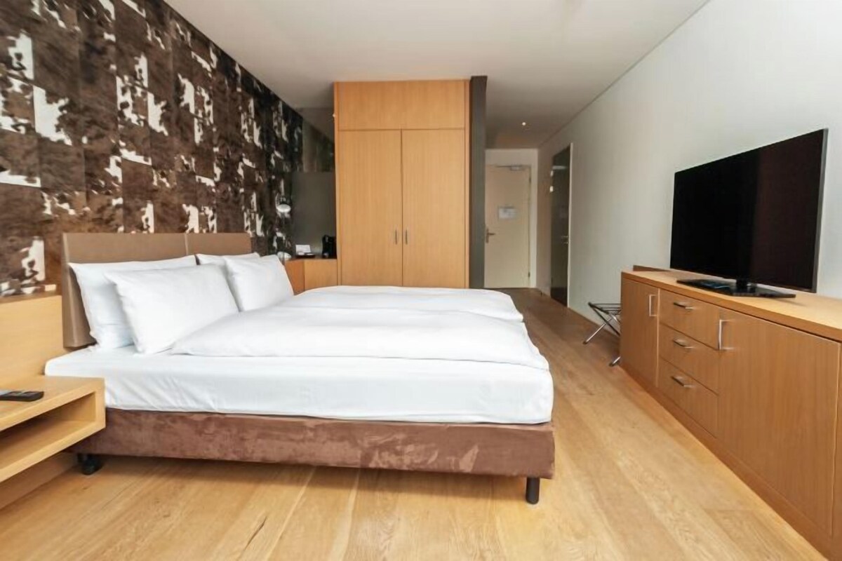A modern bedroom with a large bed, wooden wardrobe, and a television on a stand.