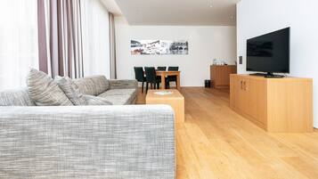 Uma sala de estar moderna com sofá, televisão, piso de madeira e área de jantar com cadeiras e mesa.