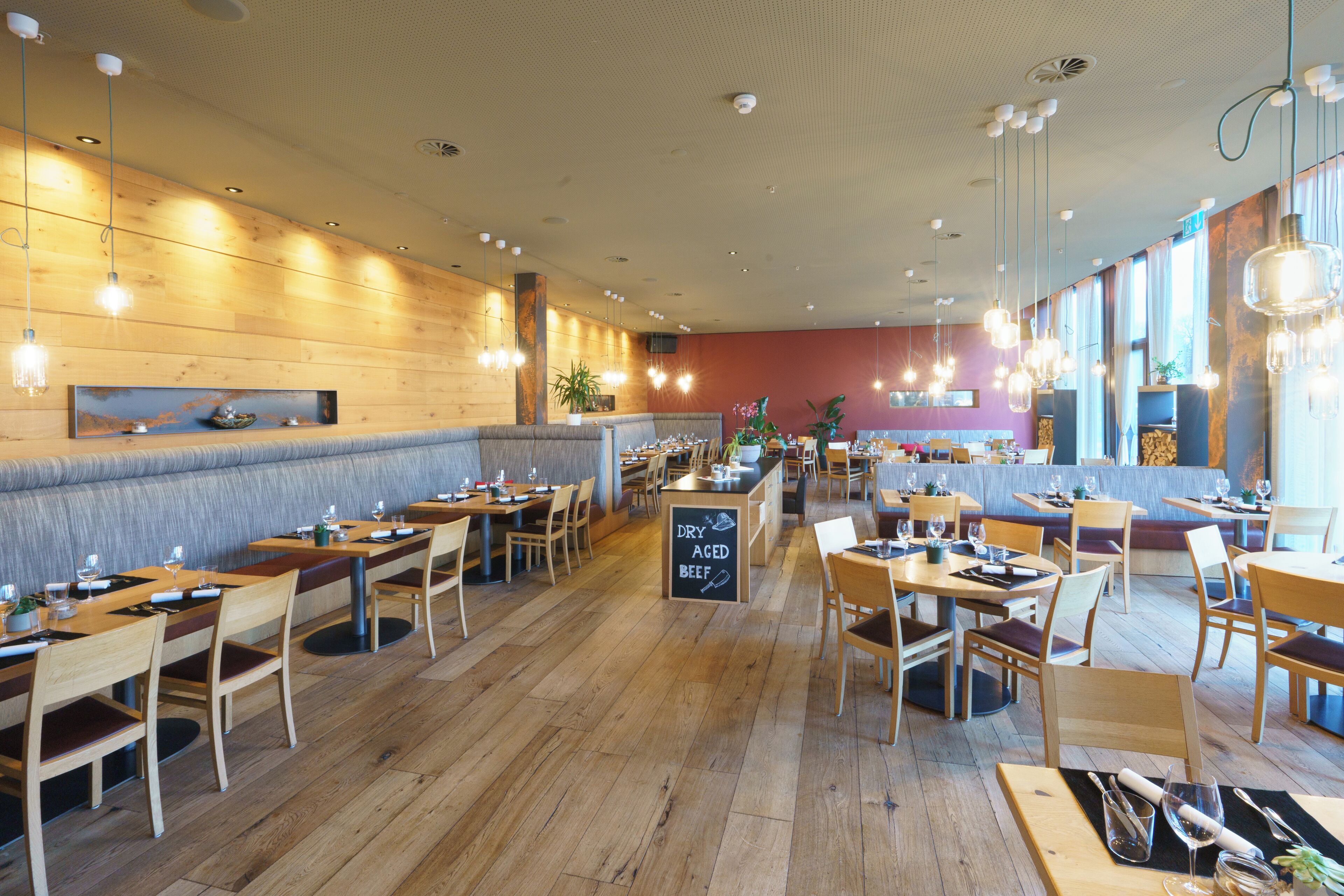 Un restaurante con mesas y sillas de madera, un menú en una pizarra y lámparas colgantes.