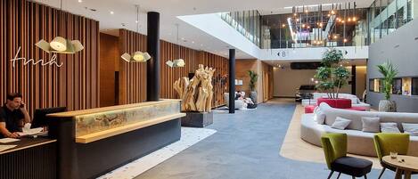 A modern hotel lobby with a reception desk, seating areas, and a staircase leading to an upper level.