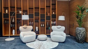 A modern living room with two white armchairs, a round rug, and a large bookshelf filled with books and decorative items. - Tailormade Hotel SIHLPARK Schindellegi (Feusisberg)