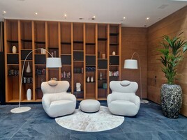 Uma sala de estar moderna com dois poltronas brancas, um tapete redondo e uma grande estante repleta de livros e objetos decorativos.