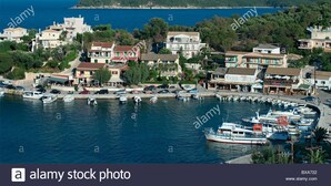 A coastal town with buildings along the waterfront, boats docked in the marina, and a mountain in the background. - The Olive Grove House, in Kassiopi with all amenities in 5 min walking distance! (Κερκυρα)