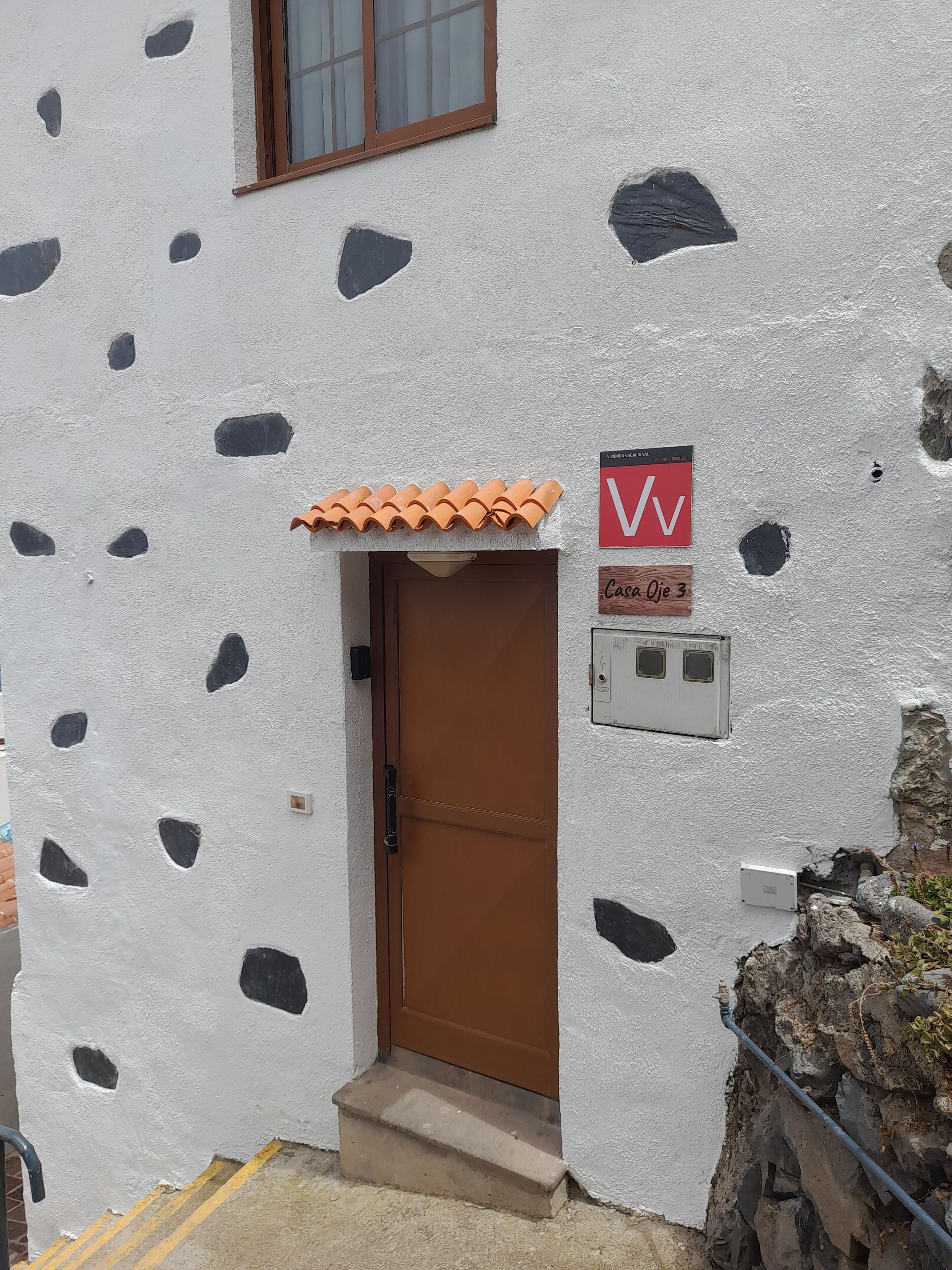 Un edificio con una puerta marrón, un letrero rojo y blanco, y un techo de tejas.