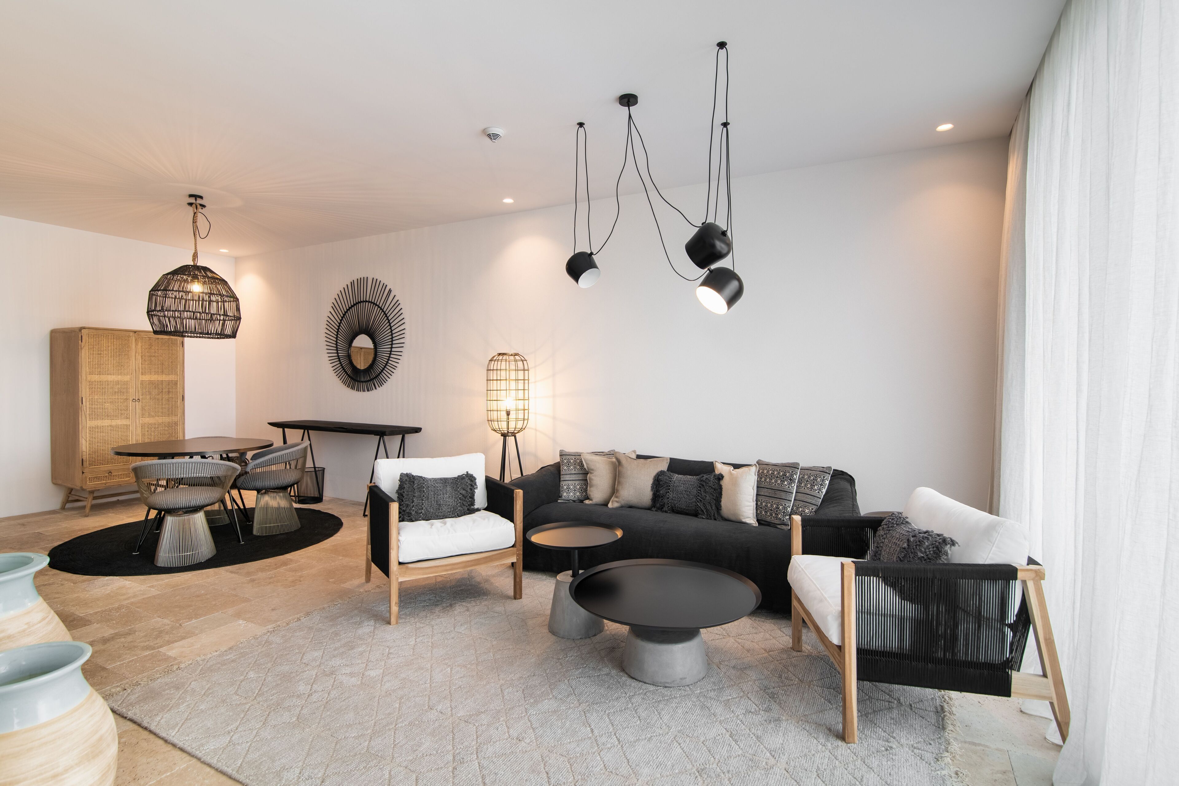 Uma sala de estar moderna com um sofá preto, poltronas brancas, uma mesa de centro redonda e um espaço de jantar com mesa e cadeiras de madeira.
