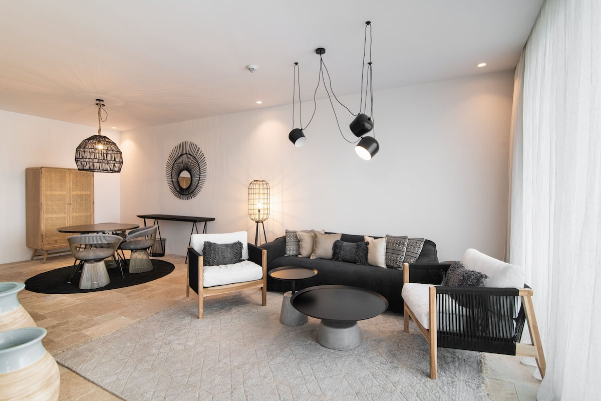 Ein modernes Wohnzimmer mit einer schwarzen Couch, weißen Sesseln, einem runden Couchtisch und einem Essbereich mit einem Holztisch und Stühlen.