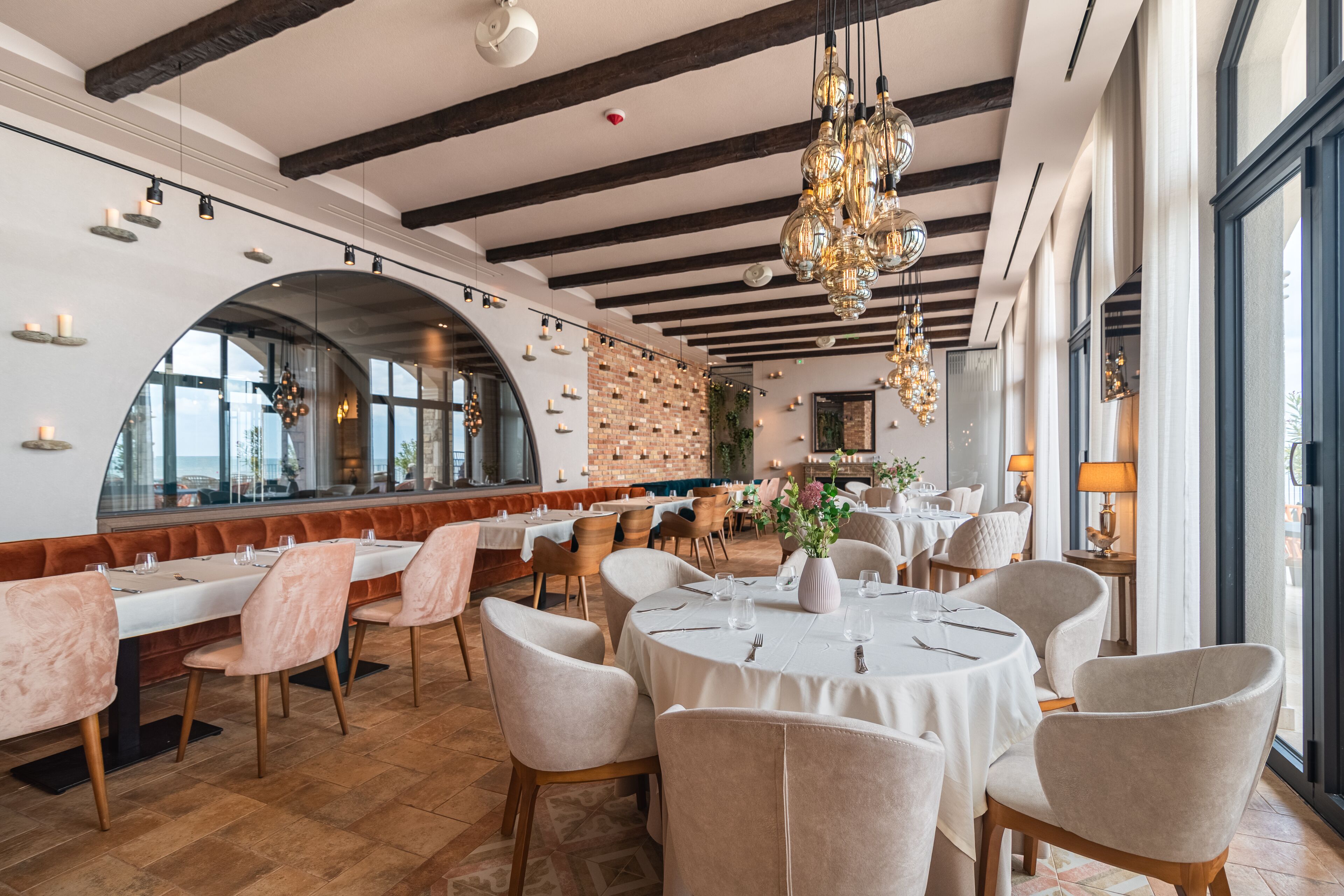 A restaurant with round tables, cushioned chairs, and a brick wall.