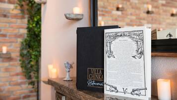 A black book titled 'Villa Chinka Restaurant' on a wooden surface with a candle and a small statue.