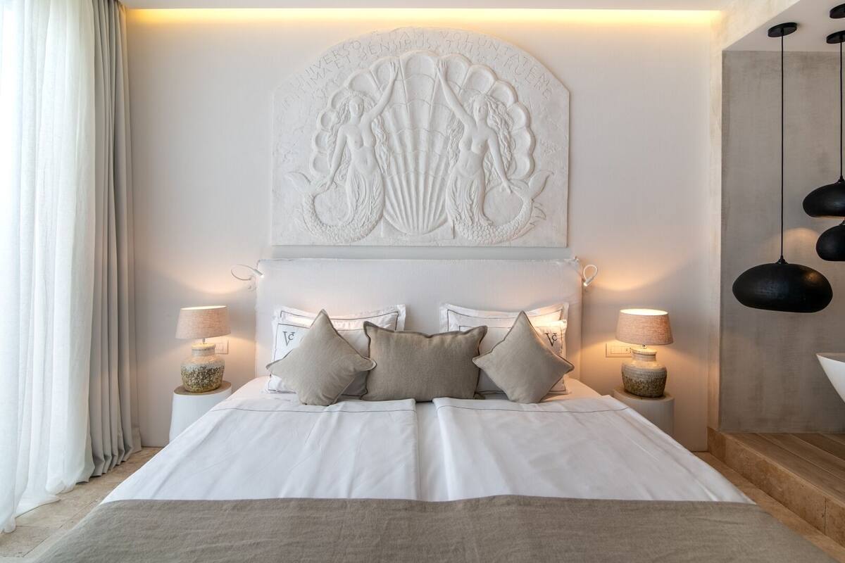 Ein Schlafzimmer mit einem großen Bett, zwei Nachttischen mit Lampen, einem dekorativen Wandbild über dem Bett und einer Hängeleuchte.