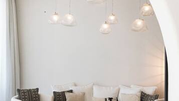 Un salon moderne avec un canapé blanc, des coussins à motifs, des tables d’appoint en bois et un design de plafond original agrémenté de luminaires suspendus.