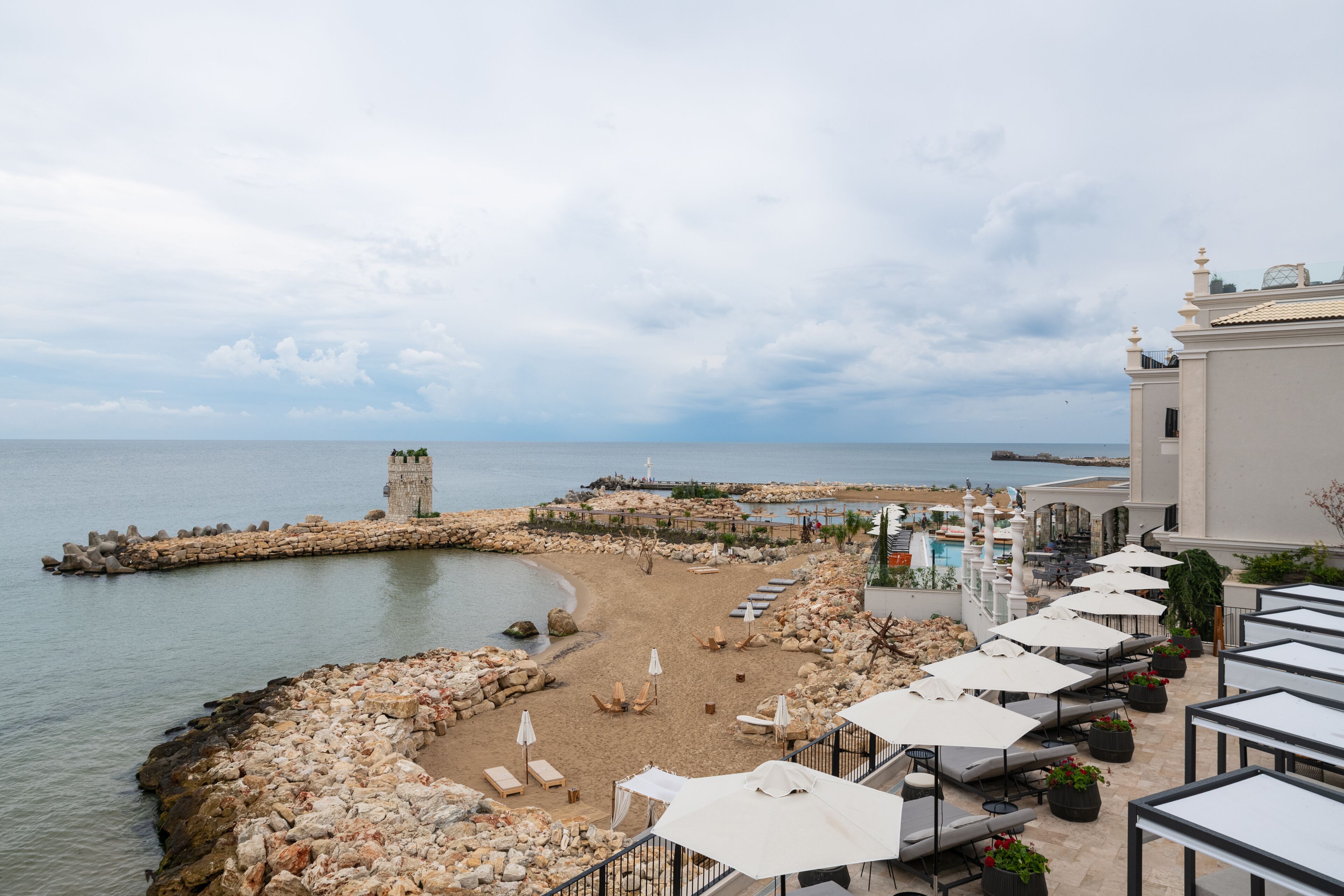 A beachside hotel with a stone pier, lounge chairs, umbrellas, and a view of the sea.