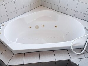 A white bathtub with four faucets and a control knob, set on a tiled floor.