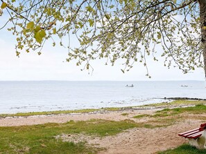 A beach with a bench, a calm sea, and boats in the distance.