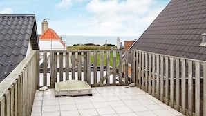 Een balkon met uitzicht op zee, een houten hek en een betegelde vloer.