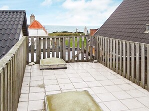 A balcony with a view of the sea, a wooden fence, and a tiled floor.