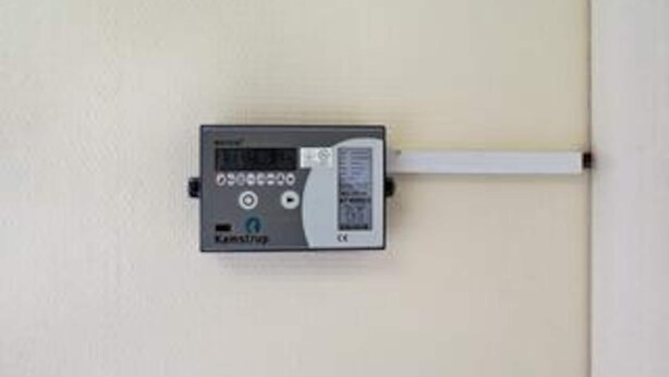 Een aan de muur bevestigd apparaat met een beeldscherm, knoppen en een kabel.