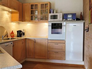 A compact kitchen with wooden cabinets, a microwave, an oven, and a refrigerator. - 4 Star Holiday Home in Lemvig (Lemvig)