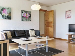 A modern living room with a sofa, a coffee table, a TV, and artwork on the walls. - 4 Star Holiday Home in Lemvig (Lemvig)