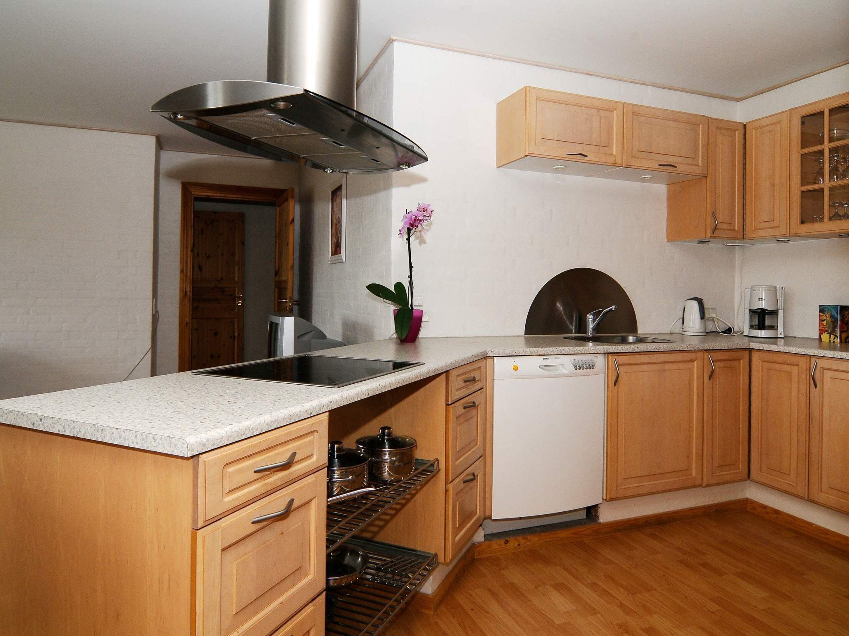 A kitchen with wooden cabinets, a stainless steel range hood, a dishwasher, and a sink.