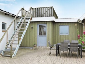 A building with a wooden staircase leading to a door, a small outdoor seating area with wicker furniture, and a potted plant. - 4 Star Holiday Home in Lemvig (Lemvig)