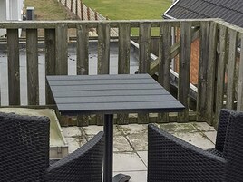 Un patio con una mesa y dos sillas, una cerca de madera y vistas a un área cubierta de césped.