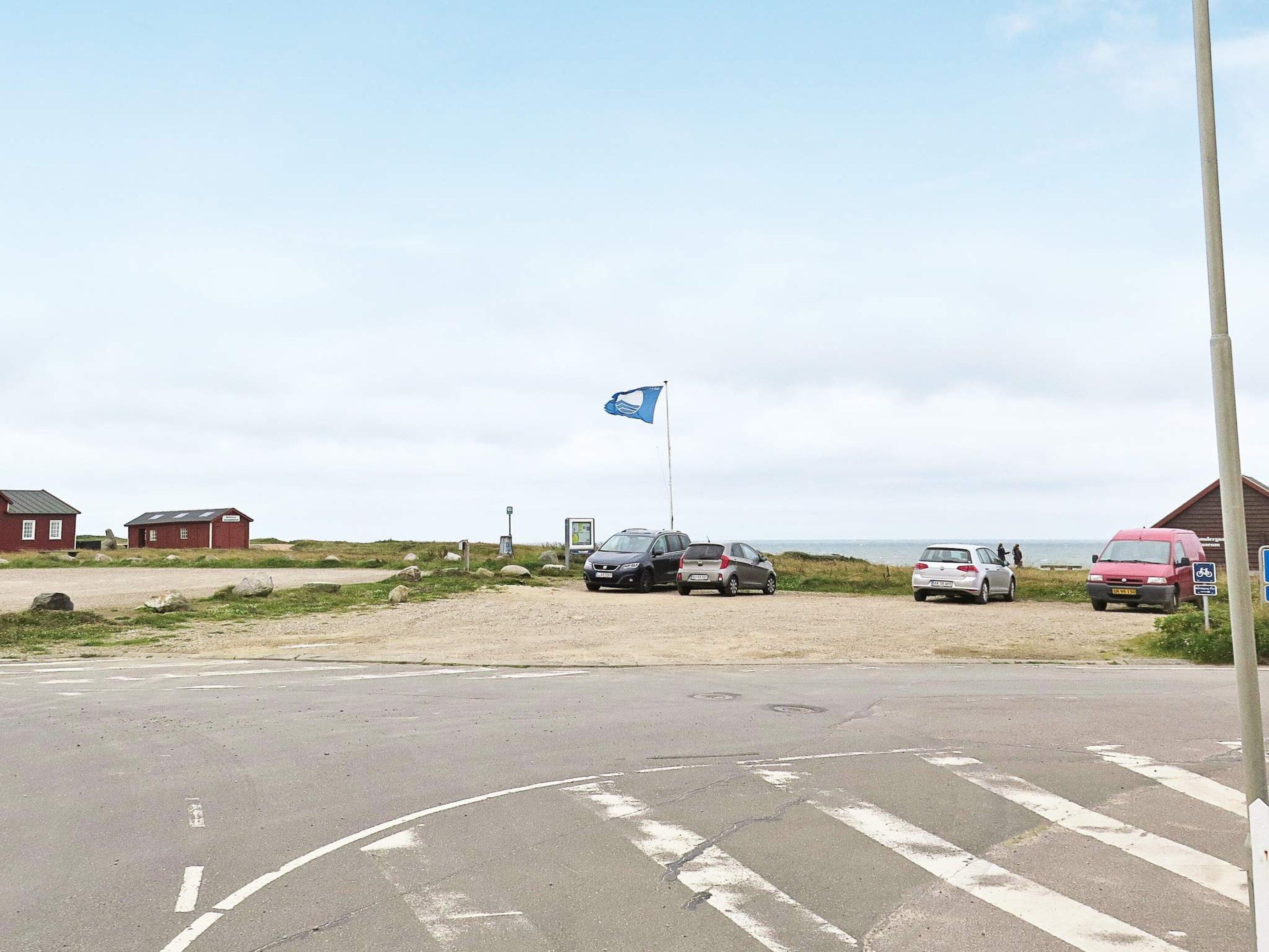 A parking area with cars, a flag, and a building in the background.