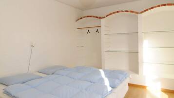A bedroom with a bed, a wall-mounted shelf, and a light fixture.