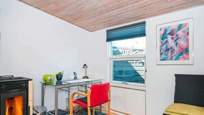 A compact living space with a glass desk, a red chair, a black sofa, a black heater, and a window with blinds. - 6 Person Holiday Home in Broager-by Traum (Broager)