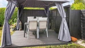 A covered patio area with a table and chairs, surrounded by a wooden fence and greenery. - 6 Person Holiday Home in Broager-by Traum (Broager)