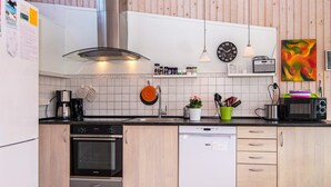 A modern kitchen with wooden cabinets, a dishwasher, a stove, and a microwave. There are hanging lights, a clock, and a colorful painting on the wall. - 6 Person Holiday Home in Broager-by Traum (Broager)