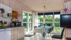 A modern kitchen with wooden cabinets, a dining area with a table and chairs, and a television mounted on the wall. - 6 Person Holiday Home in Broager-by Traum (Broager)