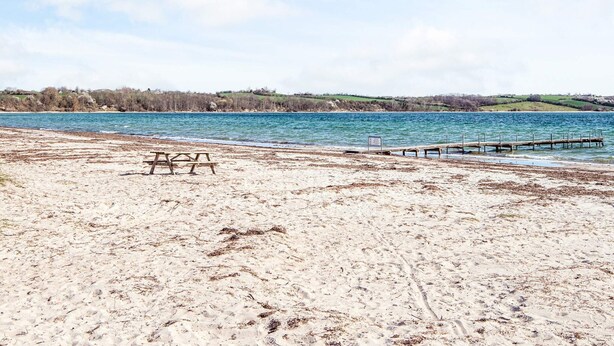 A sandy beach with a wooden picnic table and a pier extending into the water. - 6 Person Holiday Home in Broager-by Traum (Broager)