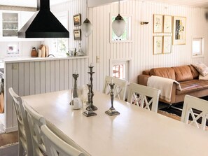 A dining area with a white table, white chairs, and a black overhead light. There is a brown leather sofa in the background. - Splendid Holiday Home in Dronningmolle near Beach (Dronningmolle)
