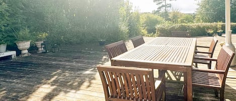 An outdoor wooden deck with a table and chairs, surrounded by greenery.