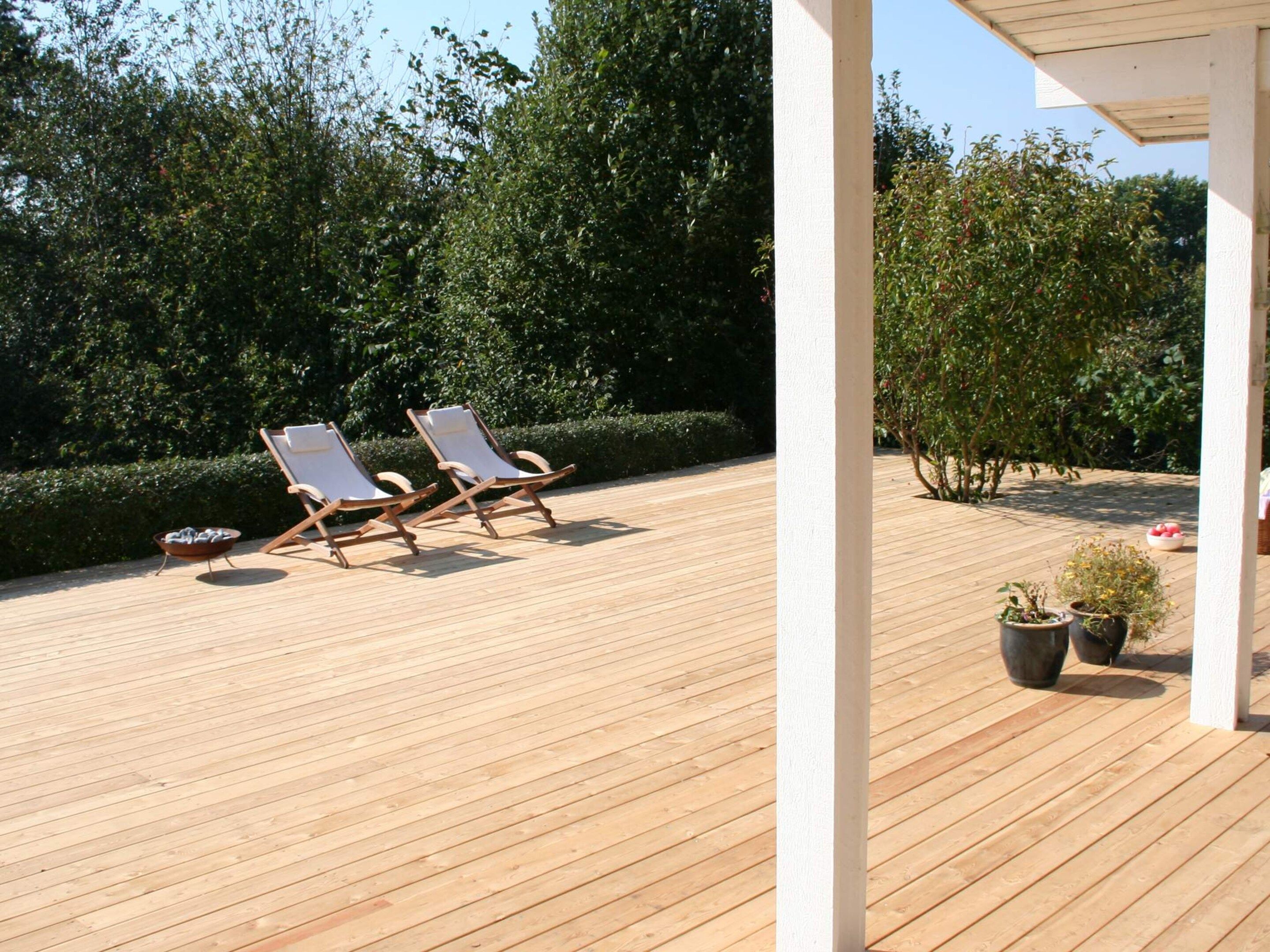 A wooden deck with two lounge chairs and potted plants.