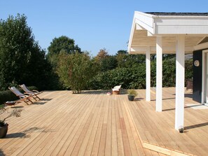 Um deck de madeira com cadeiras de descanso e área coberta.