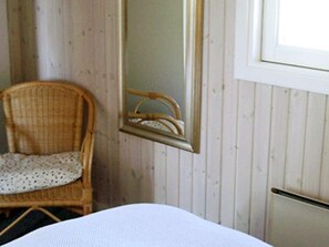 A room with a bed, a wicker chair, a mirror, and wooden paneling on the walls. - Splendid Holiday Home in Dronningmolle near Beach (Dronningmolle)